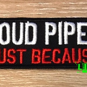 Puede incluir: Parche rectangular negro con texto bordado blanco que dice "LOUD PIPES" encima de "JUST BECAUSE" en rojo. La frase "LIVE FAST" está en verde en la parte inferior. El parche está sobre una superficie de vetas de madera.