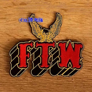 Op de afbeelding: Zwarte en rode geborduurde patch met de tekst "FTW" in een vet, gestileerd lettertype. Een gouden adelaar met uitgespreide vleugels bevindt zich boven de tekst.