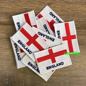 Könnte beinhalten: Ein Stapel weißer, gestickter Bügelbilder mit dem roten Kreuz der englischen Flagge und dem Wort "ENGLAND" in blauer Schrift.
