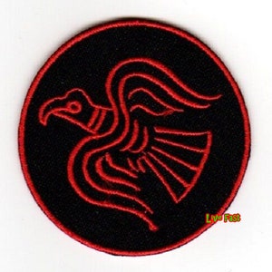 May include: A black and red embroidered patch featuring a stylized red bird with outstretched wings. The bird is surrounded by a black circle with a white outline.