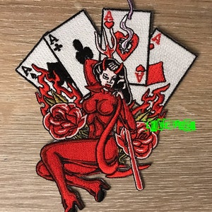 Könnte beinhalten: Gestickter Aufnäher mit einer roten Teufelsfrau mit einem Dreizack, umgeben von Flammen und Rosen. Das Design beinhaltet Spielkarten mit dem Ass von Kreuz, Karo und Herz. Der Aufnäher hat einen weißen Rand.
