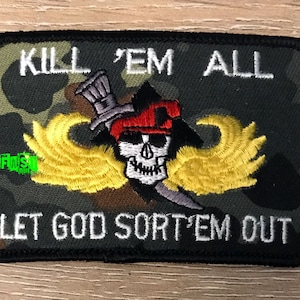 May include: A black and green camouflage patch with a white skull and crossbones design. The skull is wearing a red beret and has yellow wings. The text "KILL 'EM ALL LET GOD SORT 'EM OUT" is embroidered in white.