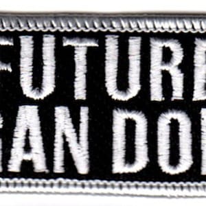 Pode incluir: Etiqueta bordada preta e branca com texto branco que diz "FUTURE ORGAN DONOR" em um fundo preto. A etiqueta tem uma borda branca.
