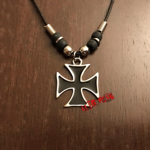 Op de afbeelding: Een ketting van zwart lederen koord met zilveren metalen kralen en een zwarte emaille kruis hanger.