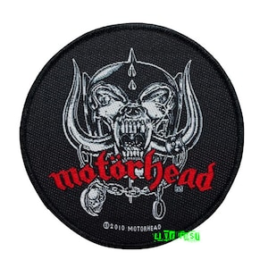May include: Black and white embroidered patch with a skull wearing a helmet and horns. The text "Motörhead" is in red lettering below the skull. The text "©2010 Motörhead" is in smaller white lettering below the red text.