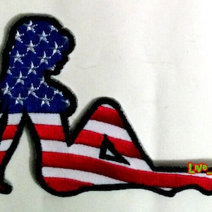 Puede incluir: Parche bordado con la silueta de una mujer reclinada, con el diseño de la bandera estadounidense. La parte superior es azul con estrellas blancas, la inferior tiene rayas rojas y blancas. El parche tiene un borde negro. Texto "Live-Fast".