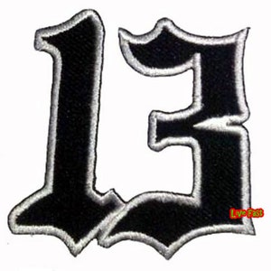 以下が含まれることがあります： ゴシック体で数字の13が刺繍された黒と白のアイロン接着パッチ。パッチは白いアウトラインがあり、幅は約7.5cmです。