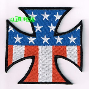 May include: An embroidered iron-on patch featuring a black iron cross with an American flag design. The flag is red, white, and blue with white stars on a blue field.