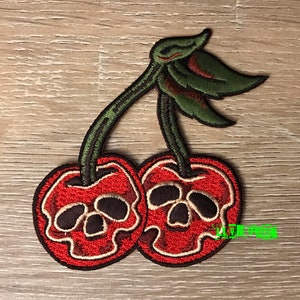 May include: Red and green embroidered patch of two cherries with skull faces.