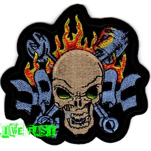 May include: Embroidered patch featuring a skull with flames, surrounded by wrenches and gears. The skull has green eyes and a menacing expression.