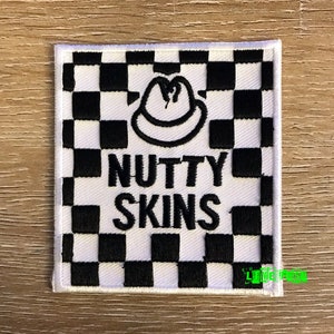 May include: White and black checkered patch with a black and white cartoon of a person wearing a hat. The text "NUTTY SKINS" is embroidered in black.