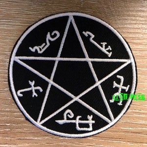 May include: Black and white embroidered patch with a five-pointed star and symbols around the perimeter. The star is white and the background is black.