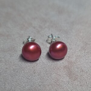 May include: A pair of silver stud earrings with round, dark red pearl accents.