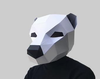 May include: A person wearing a white paper mask shaped like a bear's head. The mask has black eyes and a black nose. The person is wearing a black turtleneck sweater and has their arms crossed.