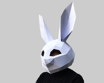 Peut inclure: Une personne portant un masque de lapin en papier mâché blanc avec des yeux noirs. La personne porte un pull à col roulé noir et a les bras croisés.