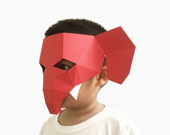 May include: A red paper elephant mask with white teeth. The mask is being worn by a child wearing a white t-shirt with the text "TEAM CLASSIC" printed on it.