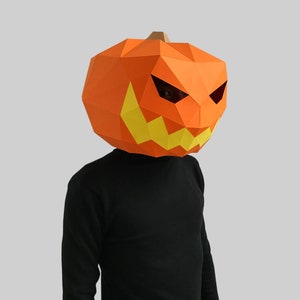Peut inclure: Une personne portant un masque de citrouille en papier m&acirc;ch&eacute; avec un visage effrayant. Le masque est orange avec des dents et des yeux jaunes.