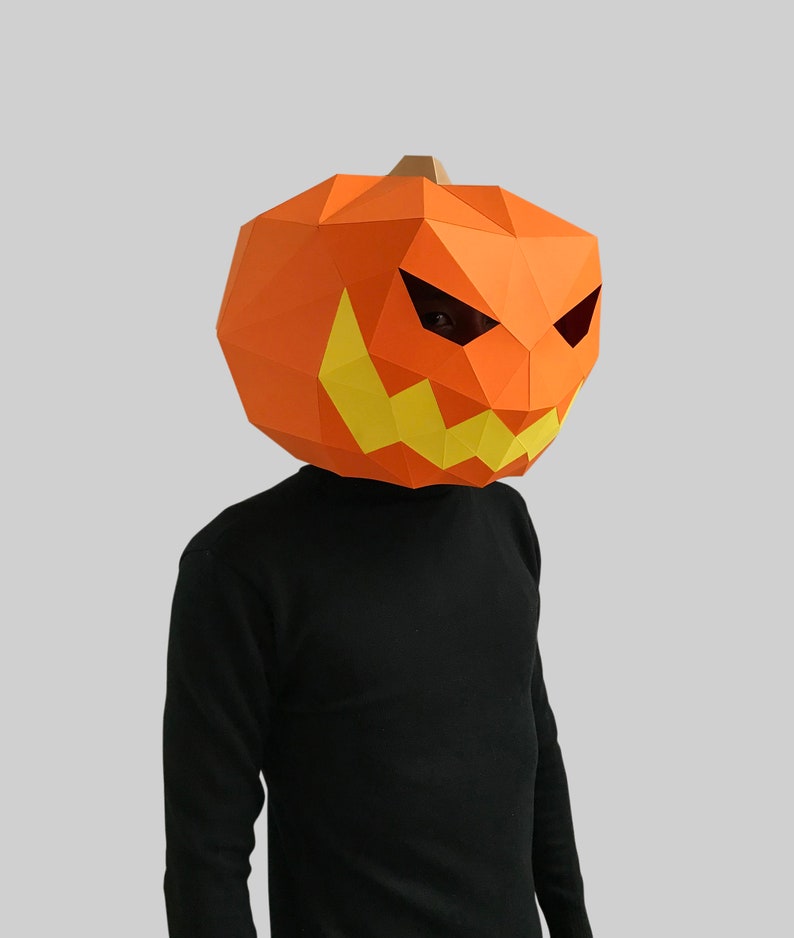 Peut inclure: Une personne portant un masque de citrouille en papier m&acirc;ch&eacute; avec un visage effrayant. Le masque est orange avec des dents et des yeux jaunes.