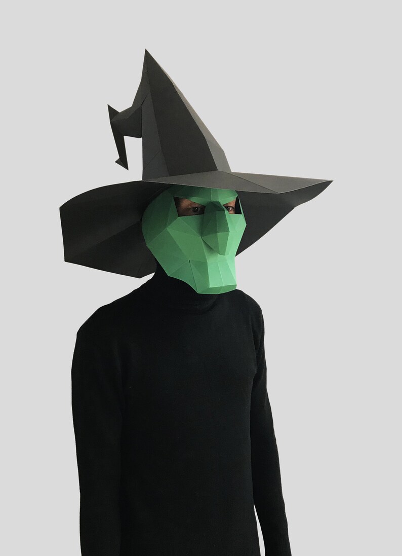 May include: A green witch mask with a black pointed hat. The mask has a large, pointed nose and a wide, open mouth.