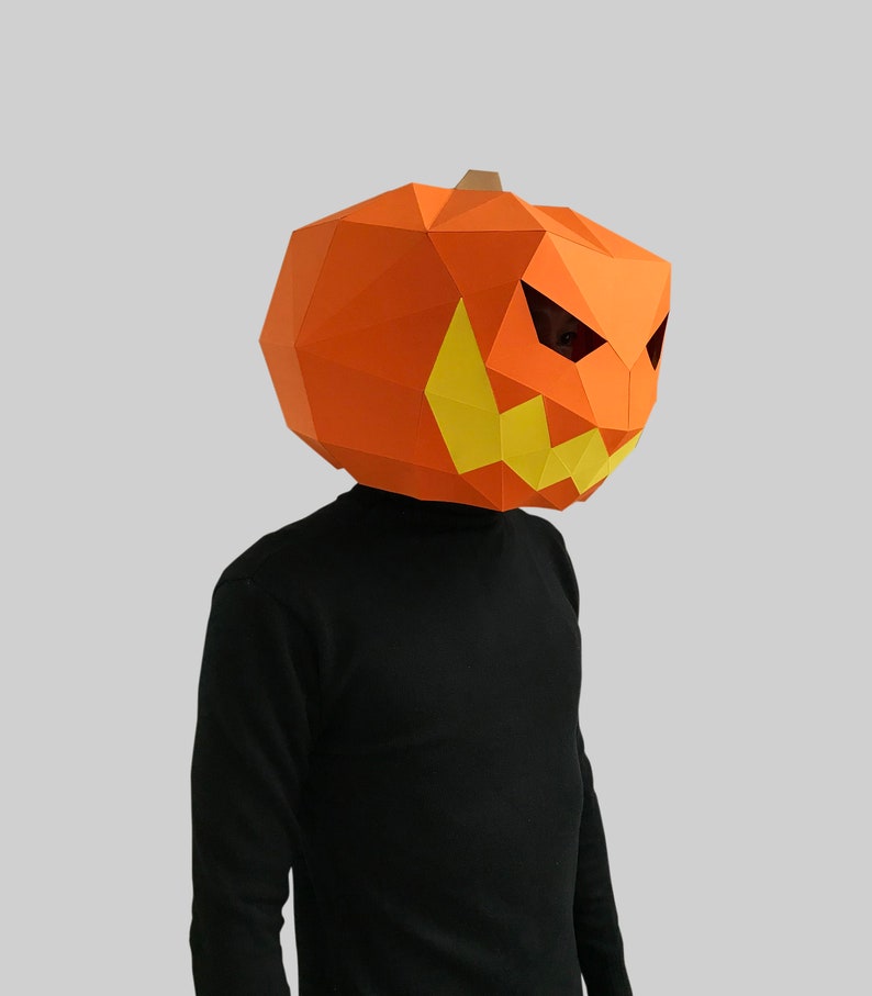 Peut inclure: Une personne portant un masque de citrouille en papier m&acirc;ch&eacute; avec un visage effrayant. Le masque est orange avec des dents et des yeux jaunes.