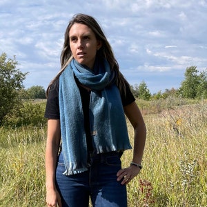 May include: A woman wearing blue jeans and a blue scarf. She is standing in a field of long grass.