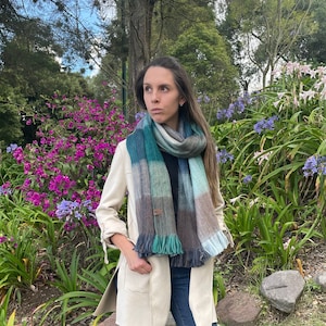 May include: A woman wearing a beige jacket, blue jeans, and black ankle boots. She is wearing a green, brown, and blue plaid scarf around her neck.