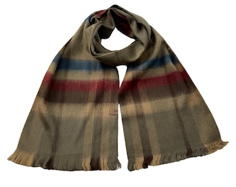May include: A rectangular scarf with a plaid pattern. The scarf features stripes of olive green, tan, burgundy, and blue. The ends of the scarf have a fringed trim. A small brown tag is sewn on the scarf.