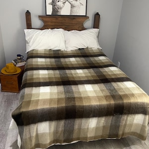 May include: A bed with a brown and tan plaid blanket. The bed has white pillows and a wooden headboard. A framed black and white photo of two alpacas kissing hangs above the bed.