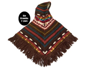 Könnte beinhalten: Ein braunes Kapuzenponcho mit einem bunten geometrischen Muster und Fransenbesatz. Das Poncho ist für Kinder von 18 Monaten bis 2 Jahren geeignet.