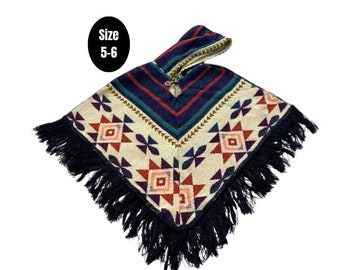 Könnte beinhalten: Ein farbenfroher gestrickter Poncho mit einem geometrischen Muster in Rot-, Blau- und Weißtönen. Der Poncho hat eine Kapuze und einen schwarzen Fransenbesatz an den Rändern. Das Größenetikett lautet "Größe 5-6".