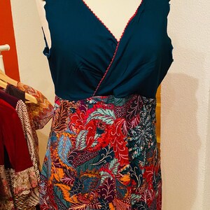 Könnte beinhalten: Ein ärmelloses Kleid mit einem blaugrünen Oberteil und einem bunten Blumenmusterrock. Das Kleid hat einen V-Ausschnitt und einen gewellten Saum.