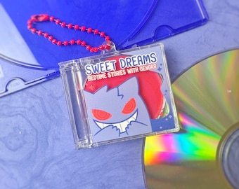 May include: A clear plastic CD case keychain with a red ball chain. The case features a cartoon Gengar design with the text "Sweet Dreams Bedtime Stories With Gengar". A CD and a blue CD case are in the background.