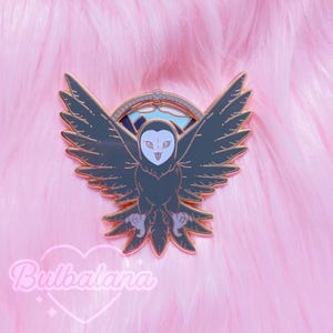 May include: A gold-tone enamel pin featuring a gray owl with a white face and open beak. The owl is flying with its wings spread wide. The pin has a blue and white mountain scene in the background.