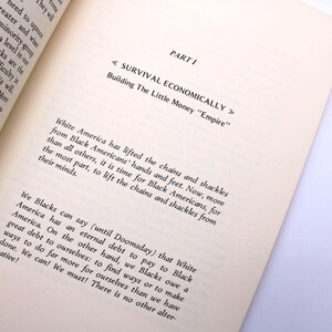 May include: An open book with text on the page. The text reads "PART I SURVIVAL ECONOMICALLY Building The Little Money Empire". The text discusses Black Americans and White America. The book is on a white surface.