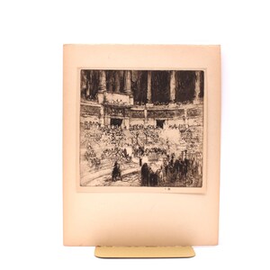 May include: A black and white etching on paper depicting a crowded interior scene with classical architectural elements, including columns and tiered seating. The artwork features numerous figures gathered in a large hall, rendered with detailed line work.