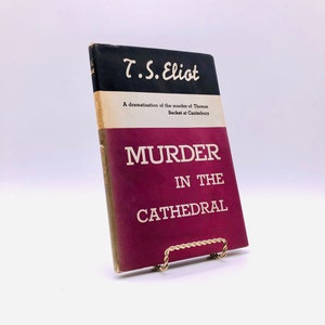 May include: A burgundy book with gold lettering on the spine. The title is "Murder in the Cathedral" by T.S. Eliot. The book is a dramatization of the murder of Thomas Becket at Canterbury.
