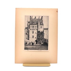 May include: A black and white etching on cream paper depicting a multi-story stone building with a steep roof, multiple chimneys, and a turret. The scene includes small figures in an open square at the base of the structure, with a signature at the bottom.