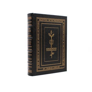 Puede incluir: Un libro de tapa dura negro titulado On the Origin of Species de Charles Darwin. La portada presenta texto dorado en relieve y un dibujo lineal central de una planta. El lomo incluye líneas horizontales doradas y el título y autor.