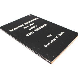 May include: A black book with the title "BLACKS' SURVIVAL For The 1980's AND BEYOND" by Dorothy C. York in white text. The book has a tan edge. The book is angled, with the title visible.