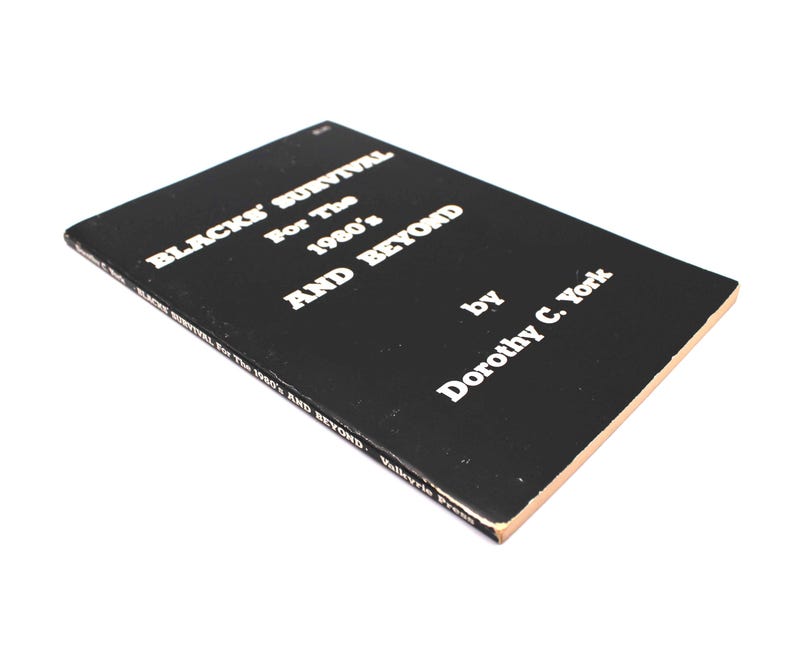 May include: A black book with the title "BLACKS' SURVIVAL For The 1980's AND BEYOND" by Dorothy C. York in white text. The book has a tan edge. The book is angled, with the title visible.