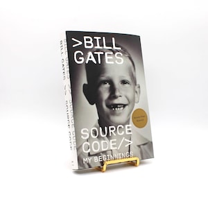 Könnte beinhalten: Eine weiße Keramik-Tasse mit schwarzem Henkel und dem Text "But First, Coffee" in schwarzer, handschriftlicher Schrift. Die Tasse steht auf einer weißen Oberfläche.
