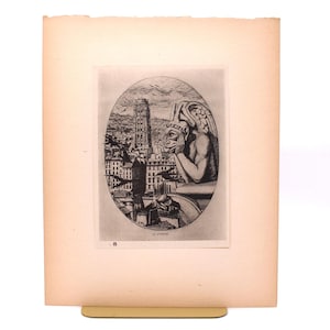 May include: An antique print featuring a detailed black and white illustration of a gargoyle overlooking a cityscape, possibly Paris. The print is set within an oval frame, with the text "LE STRYGE" at the bottom. The paper has a warm, aged tone.