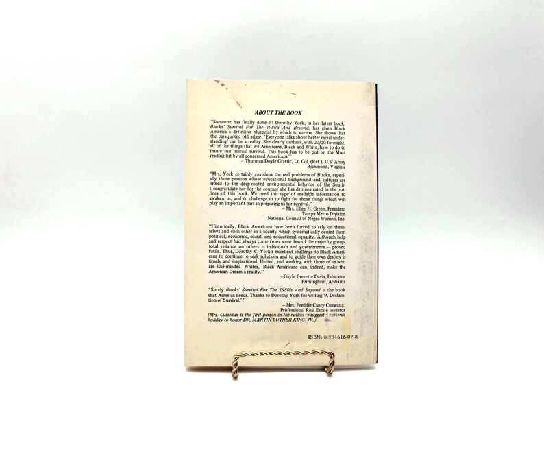 May include: A book titled "Survival For The 1990's And Beyond" by Dorothy York, with text on the back cover. The book is propped up on a gold-coloured stand. The cover features text and quotes.