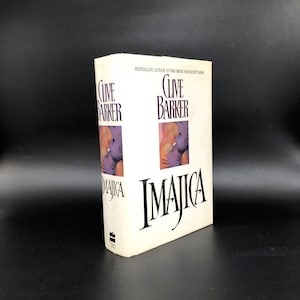 May include: A hardcover book titled "Imajica" by Clive Barker. The book has a white cover with the title in large black letters and the author's name at the top. The cover features a partial image of two figures.