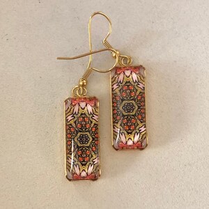 May include: Gold dangle earrings with rectangular glass charms featuring a colorful geometric pattern in shades of pink, red, gold, and black.