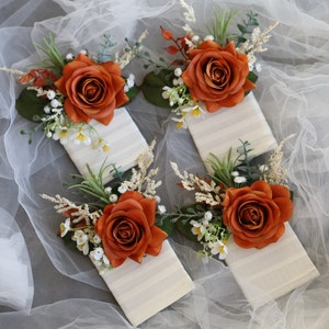 May include: Four small white gift boxes with orange roses and white flowers on top. The boxes have a striped pattern.