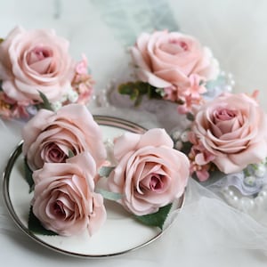 Pode incluir: Cinco botões de rosa cor-de-rosa com detalhes em pérolas e folhagem.