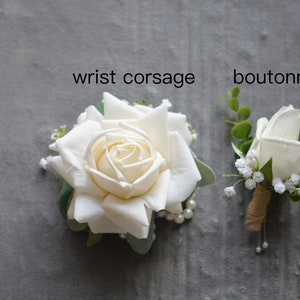 Puede incluir: Dos boutonni&egrave;res de rosas blancas, una con una sola rosa y la otra con una rosa m&aacute;s grande y detalles de perlas. El texto "wrist corsage" y "boutonniere" est&aacute; escrito sobre los arreglos.