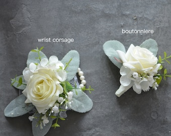 May include: Two white flower arrangements, one labeled "wrist corsage" and the other "boutonniere". Both arrangements feature white roses, small white flowers, and green leaves.
