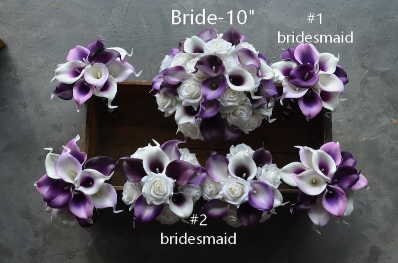 May include: A set of six bridal bouquets featuring white and purple calla lilies and white roses. The bouquets are arranged in a wooden box. The bride's bouquet is labeled "Bride-10" and the bridesmaid bouquets are labeled "#1 bridesmaid" and "#2 bridesmaid".